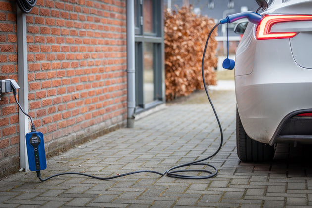 White Tesla charging at a brick house from a wallbox with a blue Voldt EV charging cable